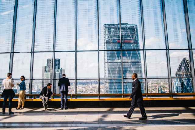 man walking on sidewalk near people standing and sitting beside curtain wall building